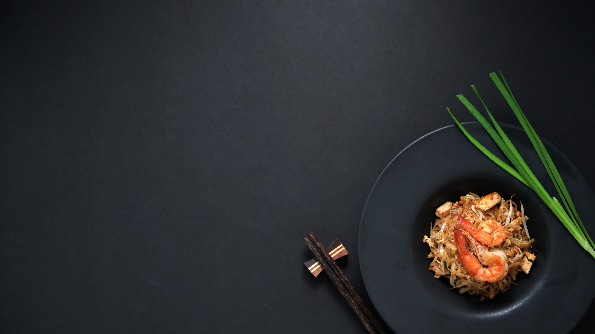 Top view of pad thai, stir fly of thai noodle with shrimp and egg in black ceramic plate on black table